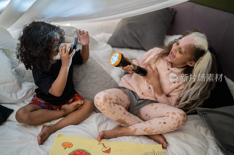 Siblings playing with binoculars and flashlight in a blanket tent at home - girl with piebaldism